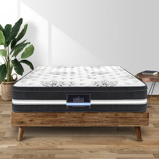 A double-sized Giselle Bedding mattress with a white and black geometric pattern on the top, placed on a wooden bed frame, with a plant and a plastic bag cutter beside it.