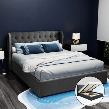 Charcoal gray upholstered queen-sized bed frame with tufted headboard and storage compartment beneath, set in a room with dark blue walls and a wooden floor.
