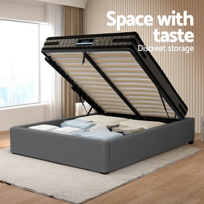 Gray bed with open storage compartment in a room with a window and curtains.