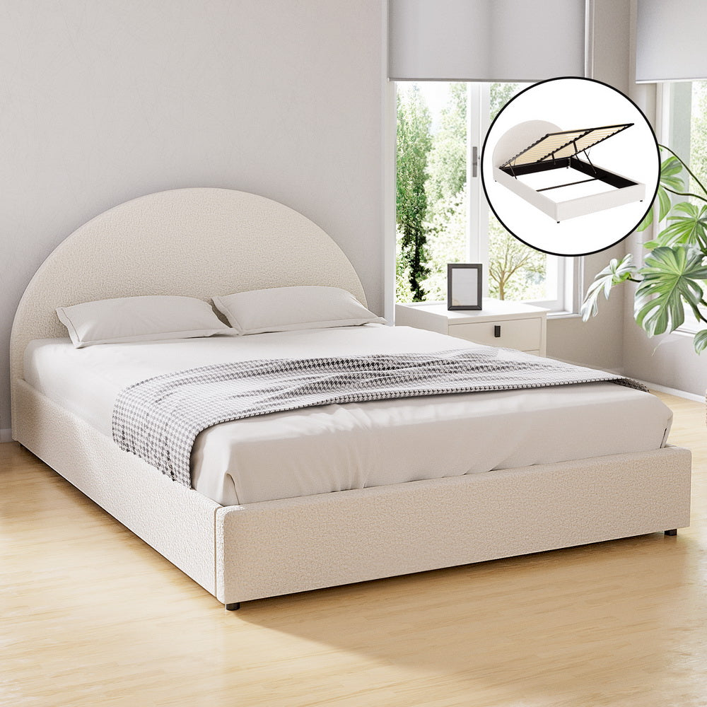 White upholstered bed with round headboard in a bright room with large windows.