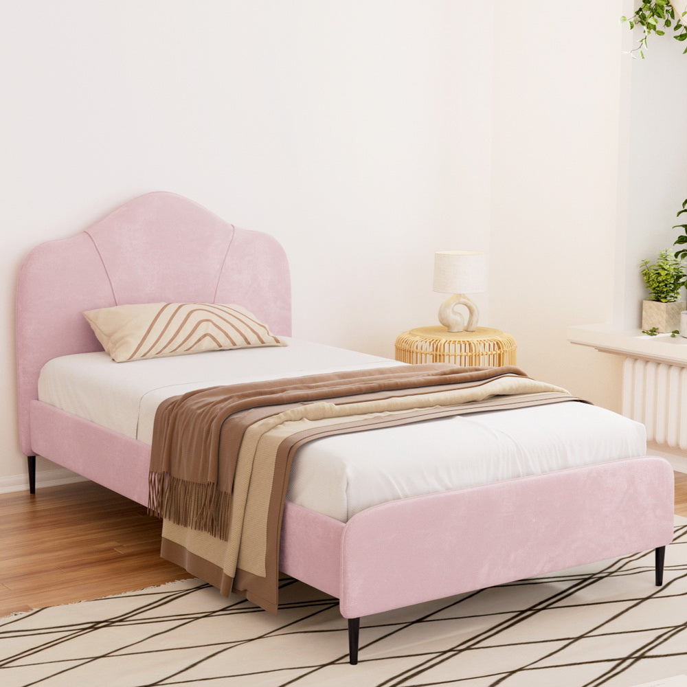 A king single sized bed frame upholstered in pink velvet fabric, with a solid headboard and metal connectors.