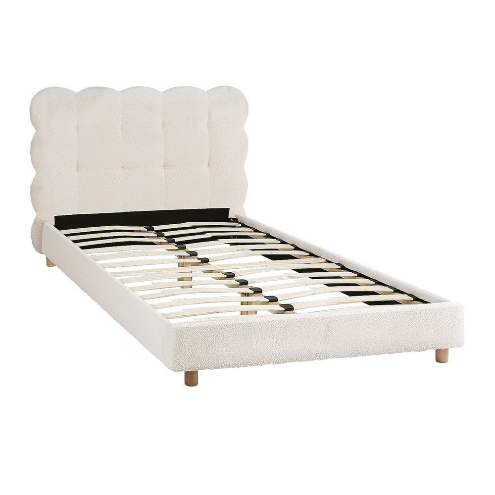 White upholstered bed with scalloped headboard on a white background