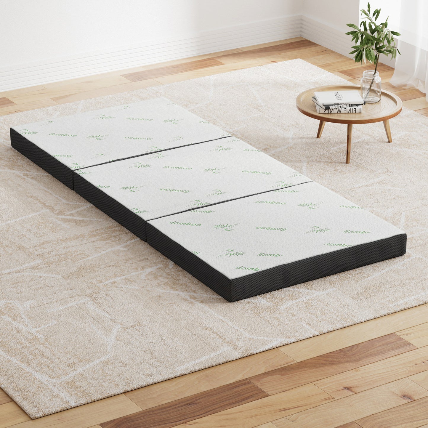 A foldable foam mattress with bamboo fabric top, displayed in a folded configuration on a rug in a living room setting, with a decorative pattern on the mattress surface.