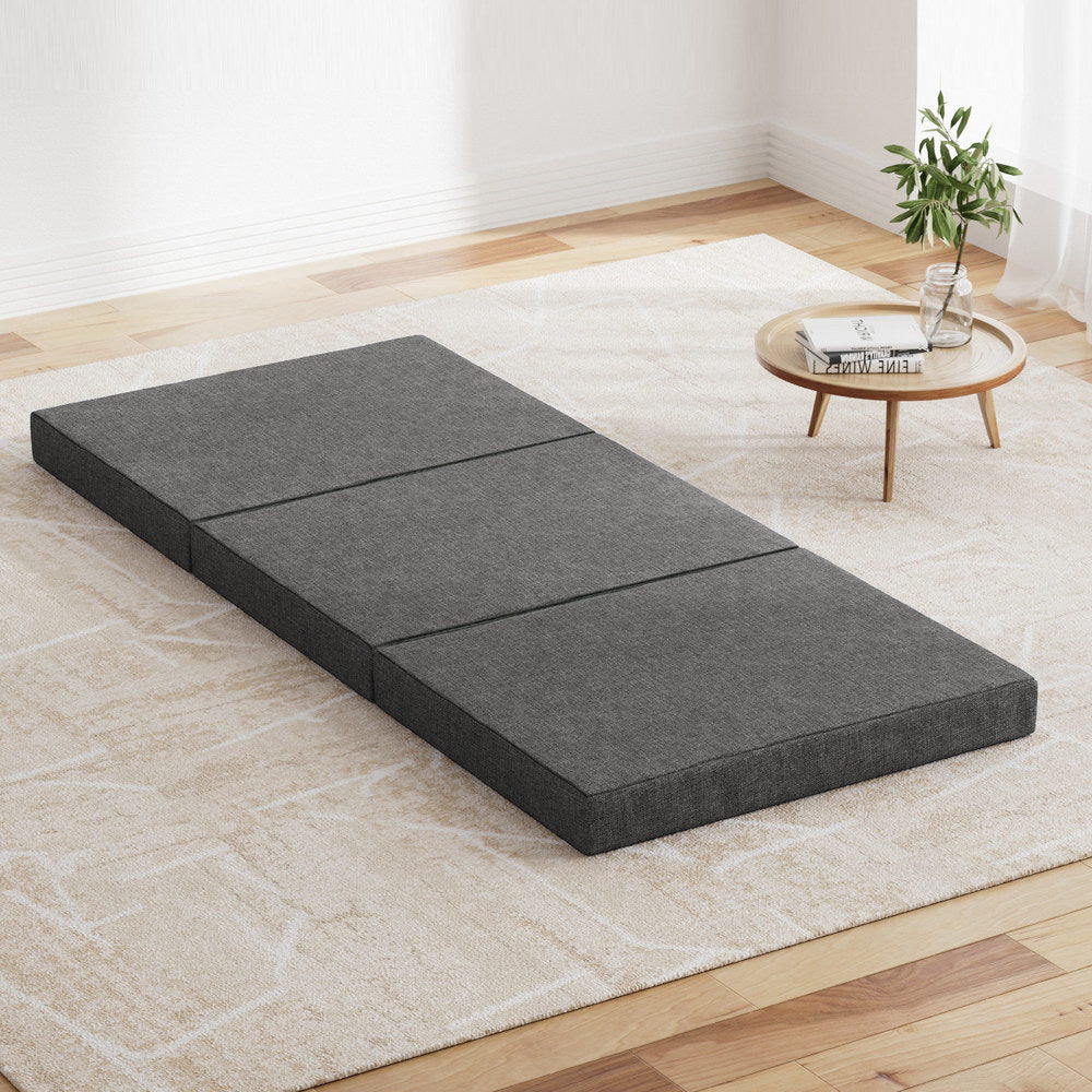 A foldable grey mattress on the floor, divided into sections, with a removable cover.
