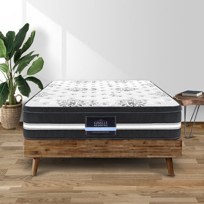 A king single sized mattress with a white and blue pattern on the top, placed on a wooden bed frame, with a plant and a nightstand in the background.