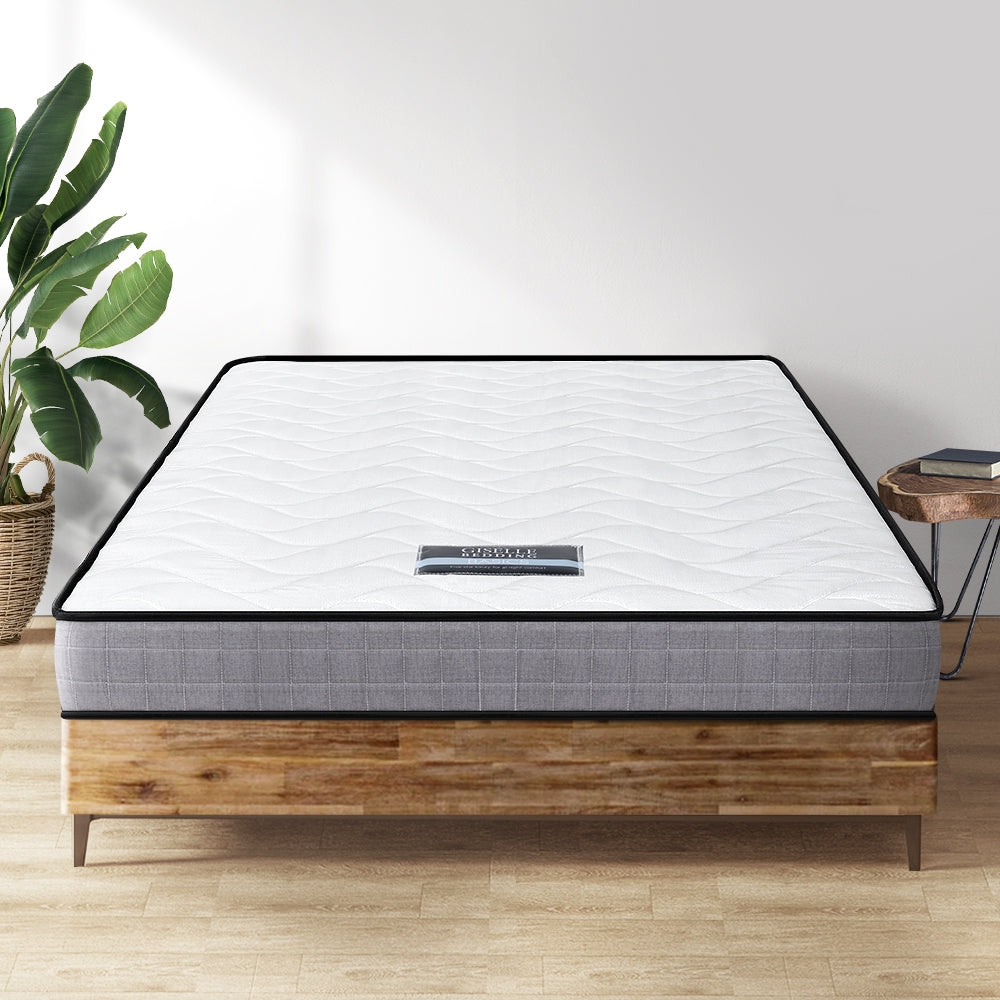 Single-sized mattress with a white quilted top on a wooden bed frame, with a decorative plant beside it.