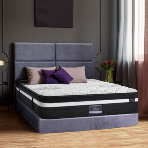 A double-sized mattress with a super firm structure, displayed in a bedroom setting with a grey headboard and colorful bedding.