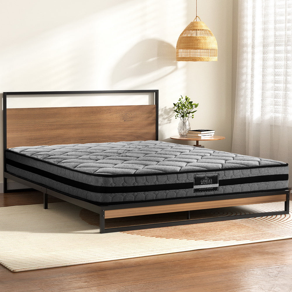 Gray mattress on a wooden bed frame in a room with a lamp and books.