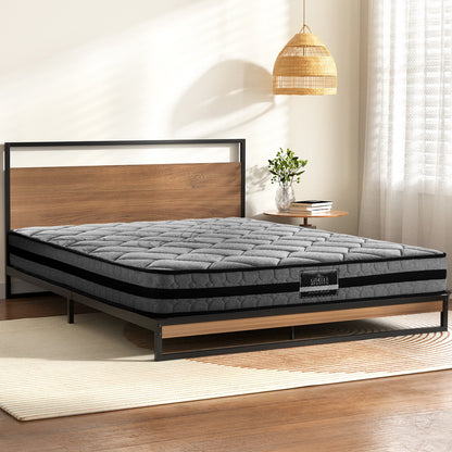 Gray mattress on a wooden bed frame in a room with a lamp and books.