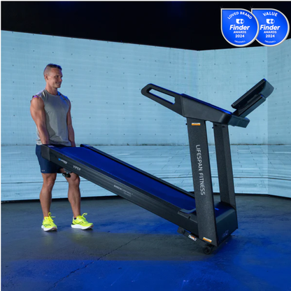 Man standing next to a LifeSpan Fitness treadmill in a room with a blue wall.