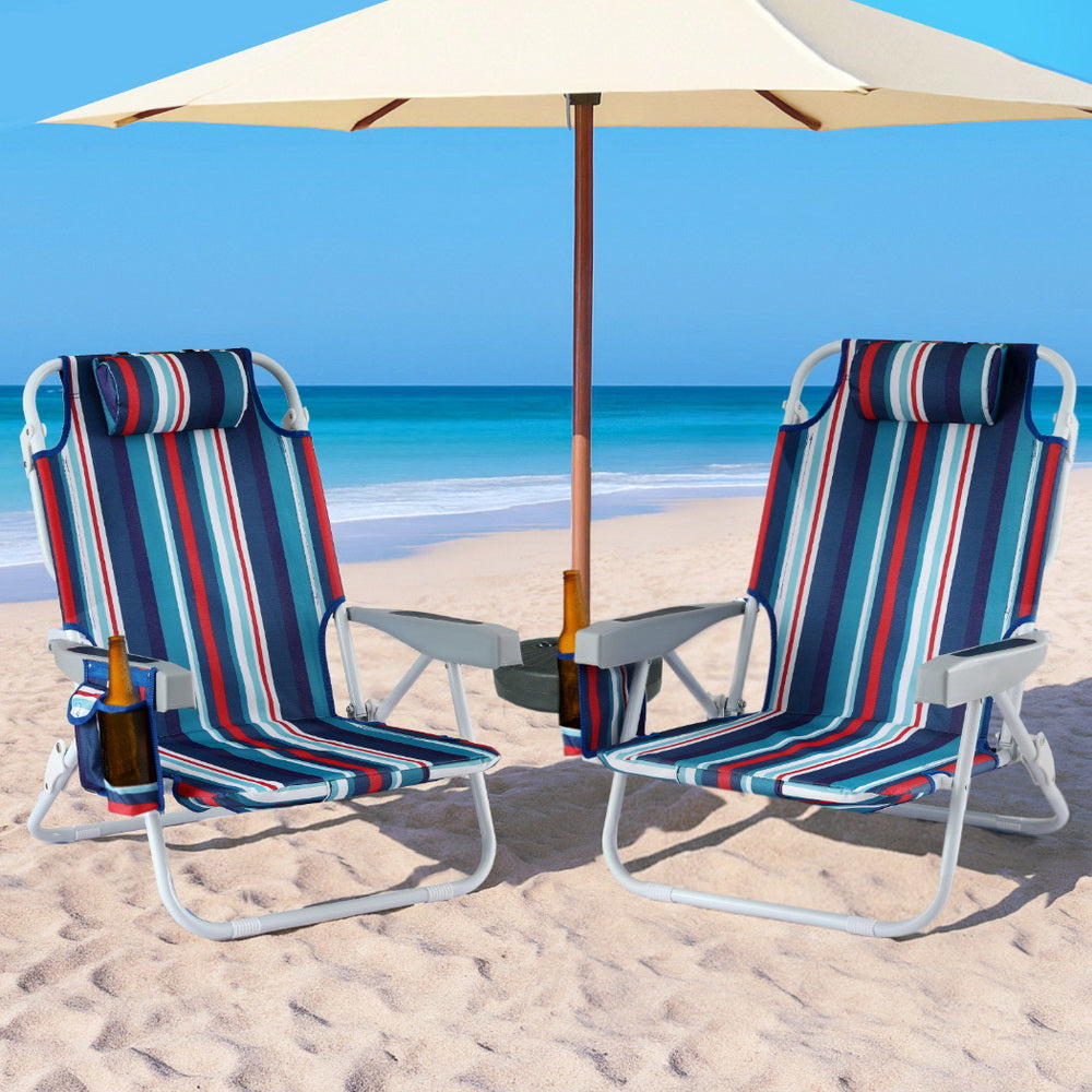 Two striped beach chairs with an umbrella on a sandy beach.