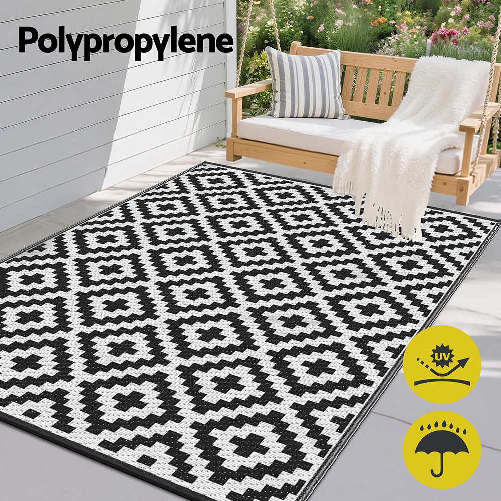 Black and white patterned outdoor rug on a patio with a swing and garden in the background, featuring Polypropylene text.