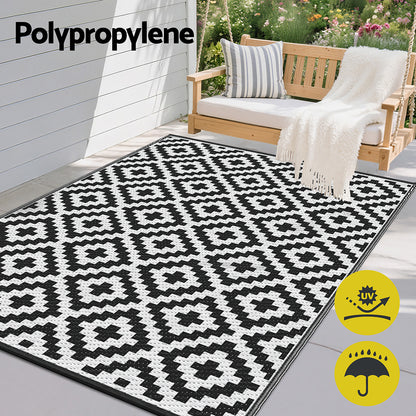 Black and white patterned outdoor rug on a patio with a swing and garden in the background, featuring Polypropylene text.