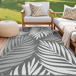 Outdoor seating area with a gray and white leaf-patterned rug, wooden chairs, and a woven ottoman.
