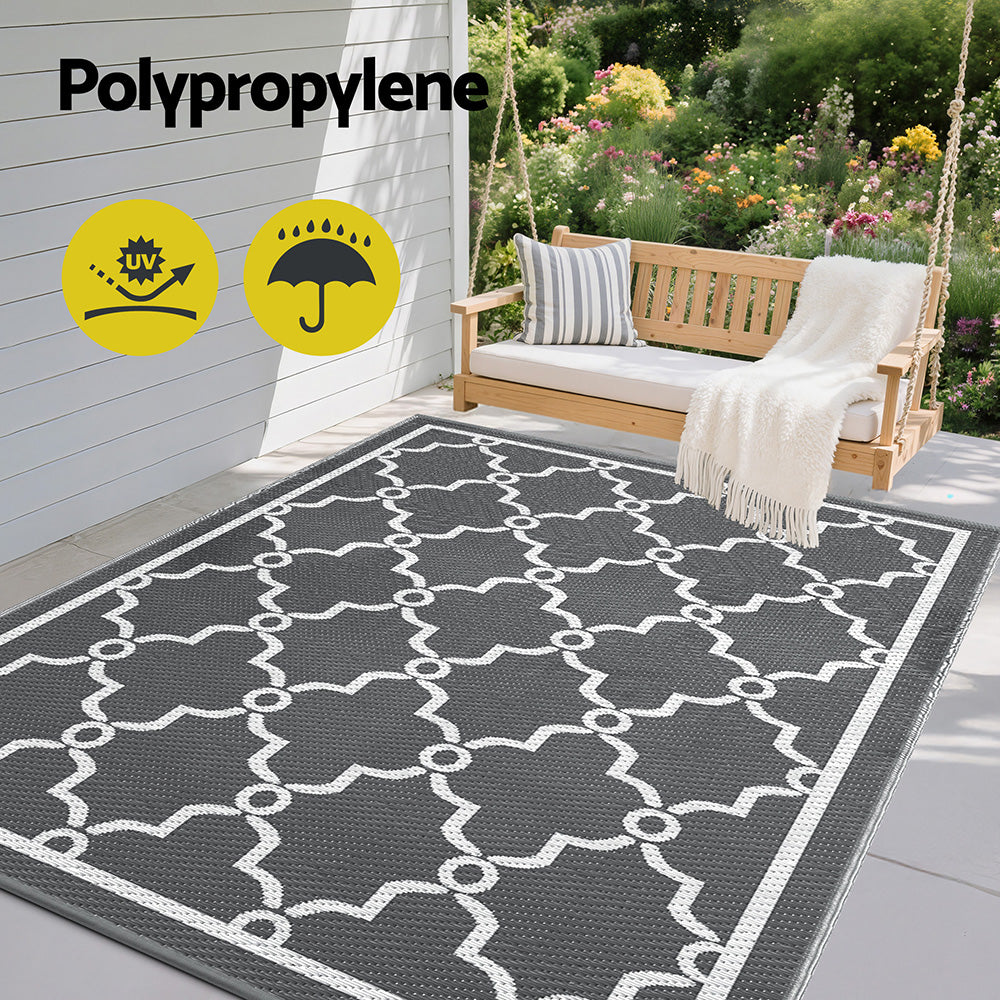 Outdoor rug with geometric pattern on a patio, featuring Polypropylene text and icons.