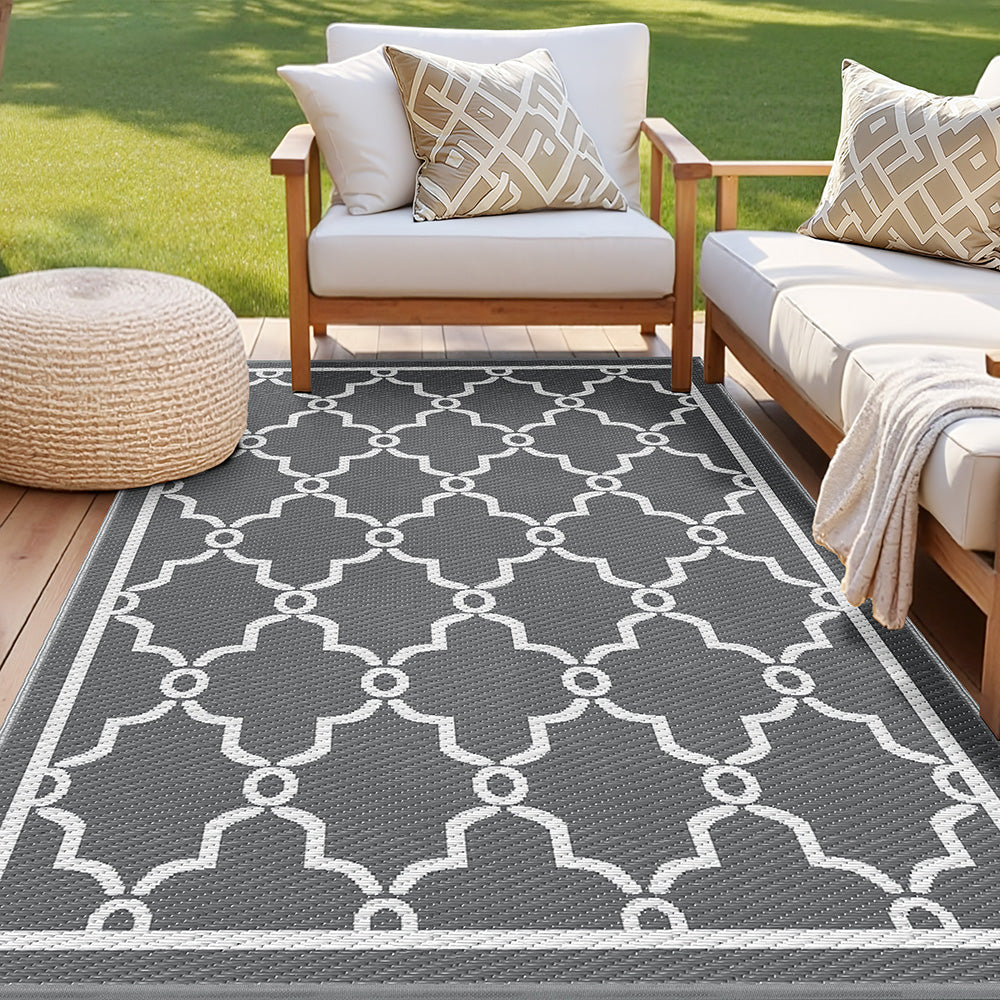 Gray outdoor rug with white pattern in front of a wooden chair and ottoman on grass.