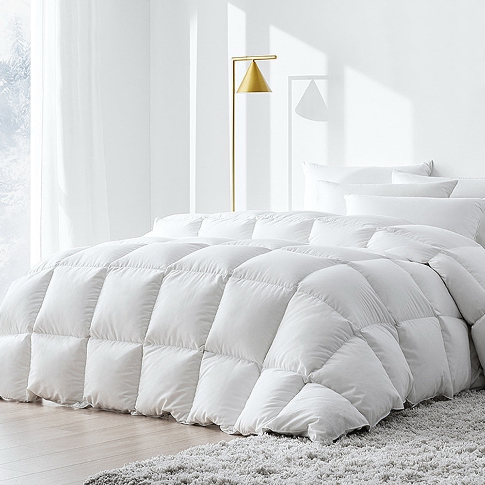 A white duck down feather quilt on a bed, with a modern bedside lamp beside it, set in a bright room.