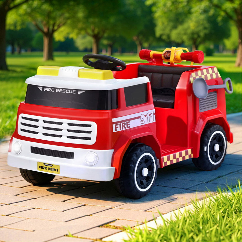 Red toy fire truck on a paved path with green grass and trees in the background