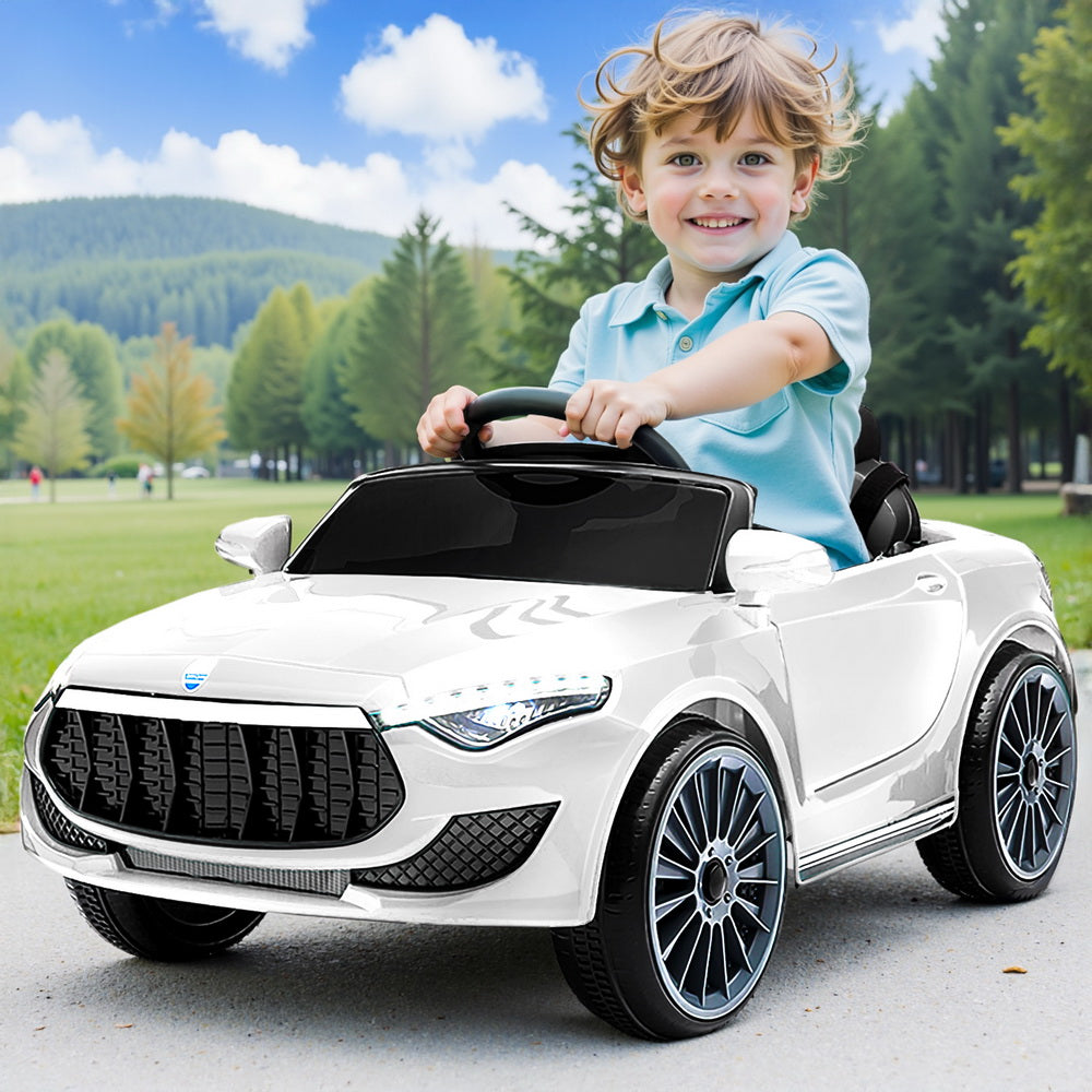 Child driving a white toy car in a park with trees and mountains in the background