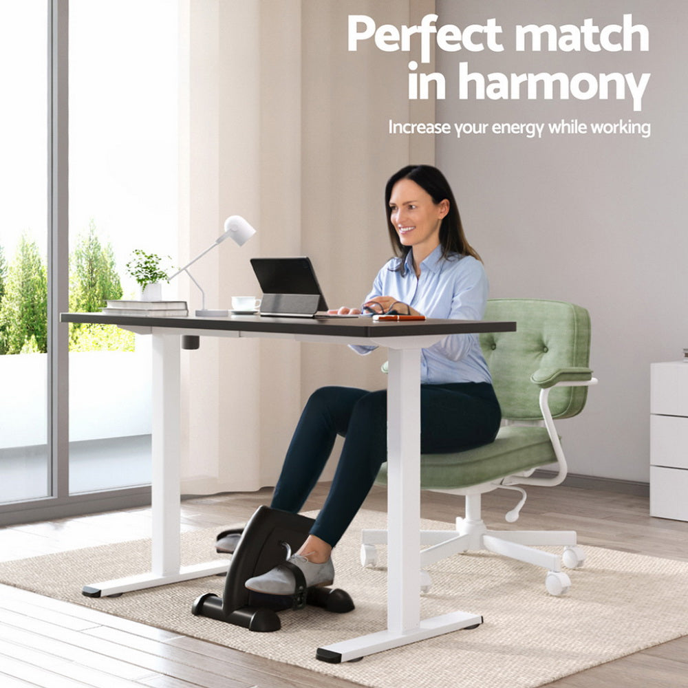 Woman using a standing desk with an exercise bike attachment in a modern office setting.