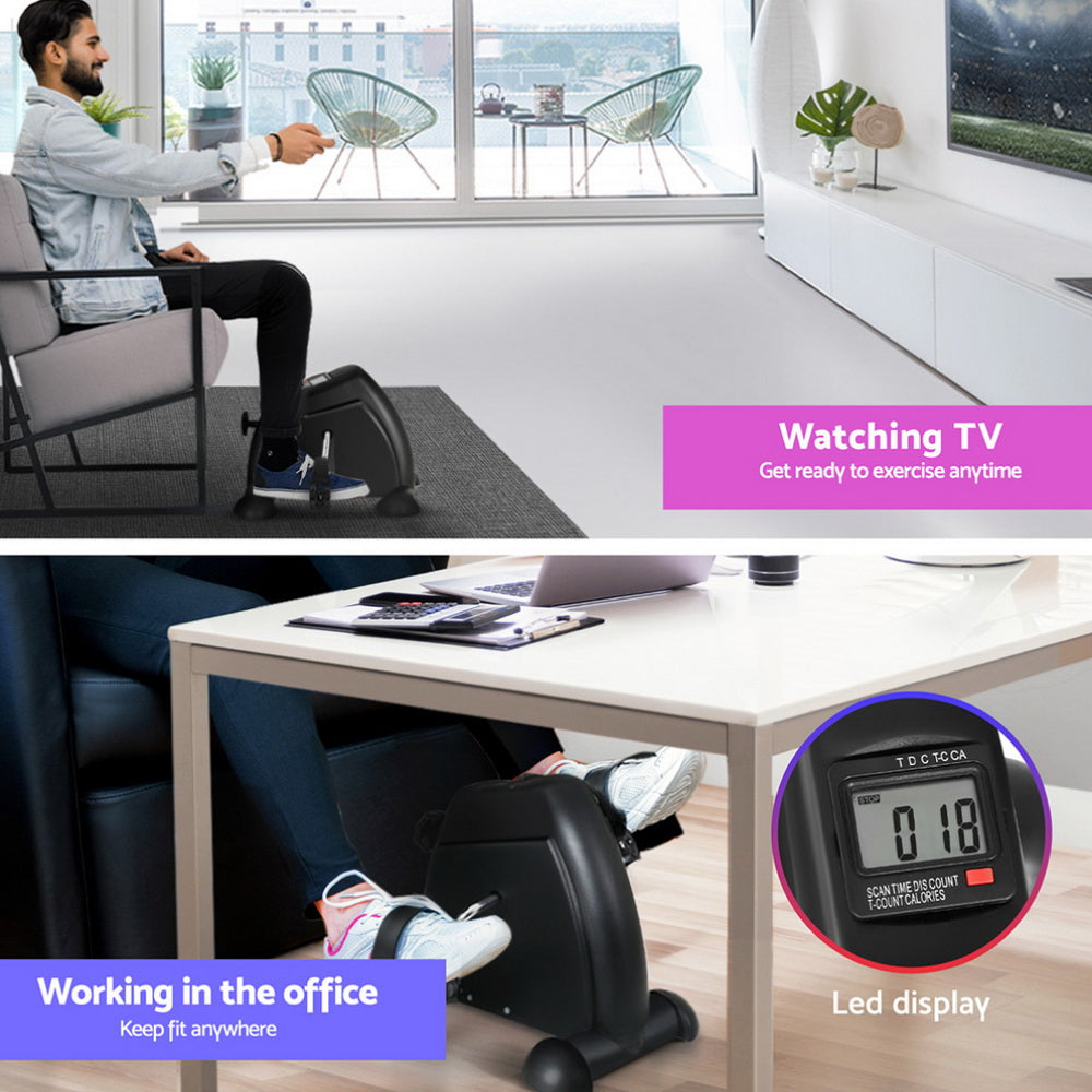 Person using a mini exercise bike in an office setting with a digital display.
