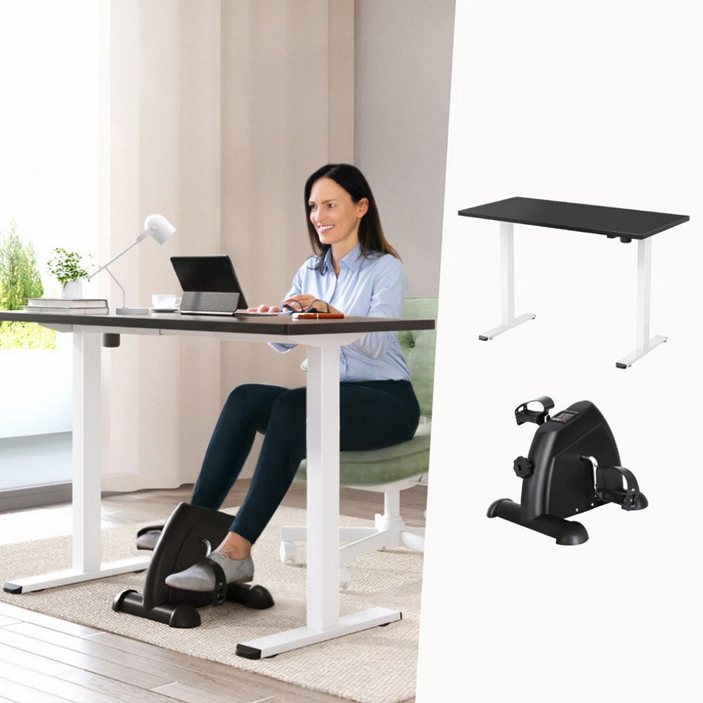 Woman using a standing desk with a small exercise bike attachment, with additional exercise bikes displayed.