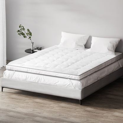 A queen-sized white mattress topper on a bed with a white bedsheet, pillows, and a plant beside the bed.