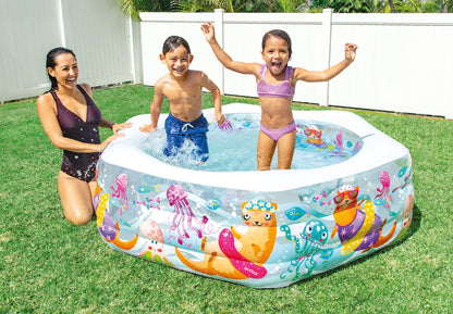 Children playing in an inflatable pool with cartoon designs on a grassy area.