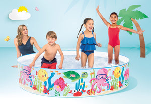 Children playing in a colorful inflatable pool with a cartoon design, surrounded by palm trees and a blue sky.