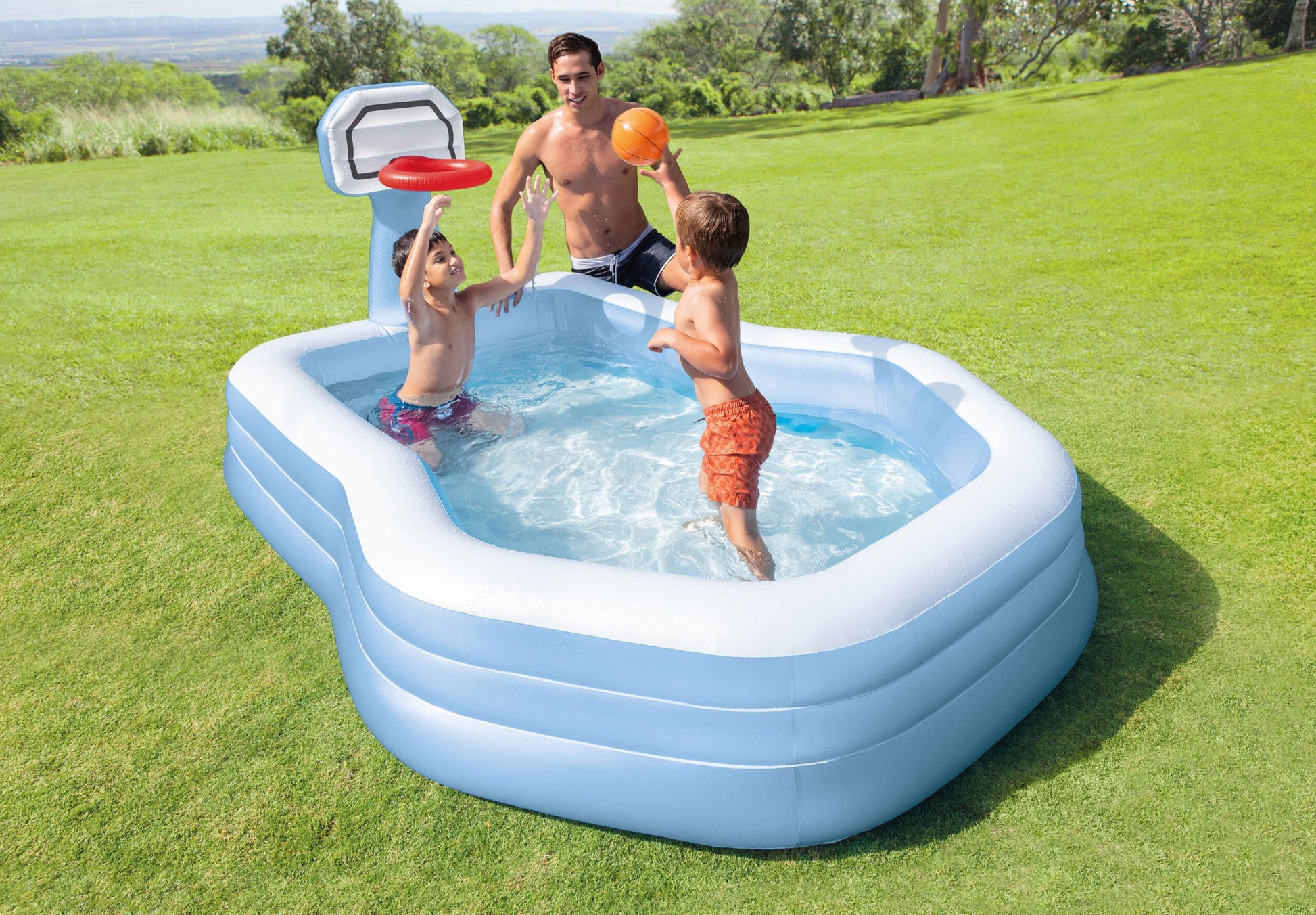 Inflatable pool with basketball hoop and children playing in a grassy area