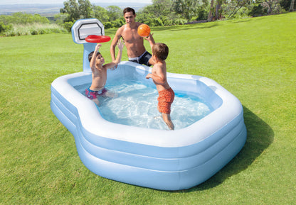 Inflatable pool with basketball hoop and children playing in a grassy area