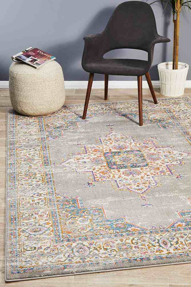 A grey rectangular Rug Culture rug featuring a traditional geometric pattern, placed on a floor with a chair and a pouf in the background.