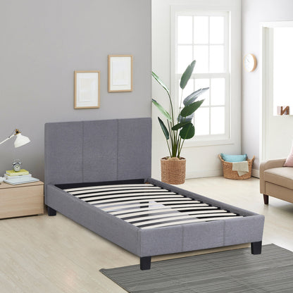 Gray upholstered bed in a room with a window, plant, and furniture.