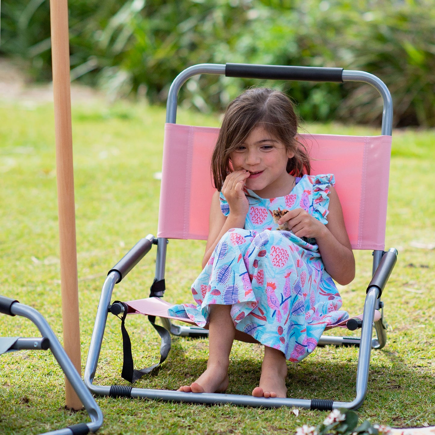 Young girl sitting on a pink and gray folding chair outdoors.