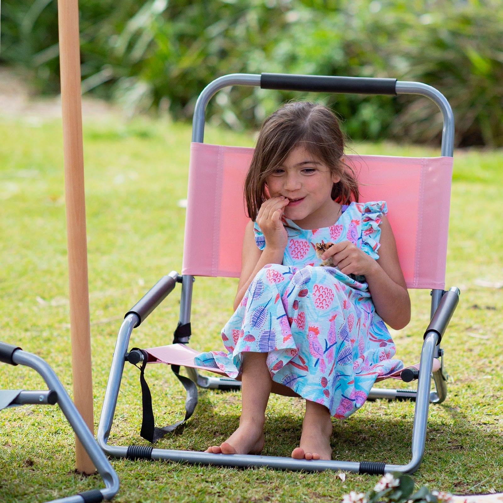 Young girl sitting on a pink and gray folding chair outdoors.