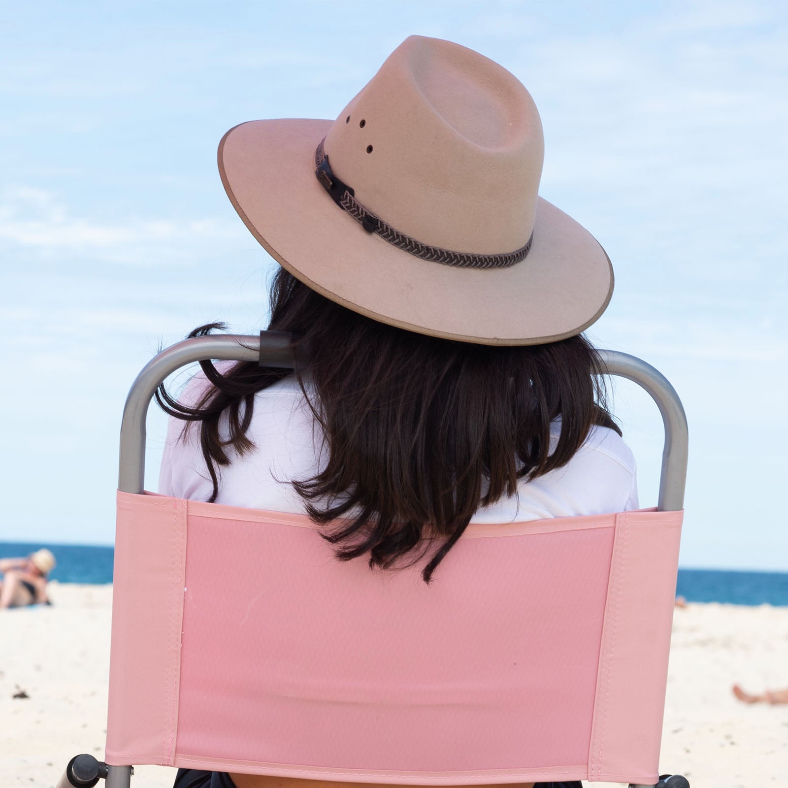 Person sitting on a beach chair wearing a wide-brimmed hat with a scenic background.