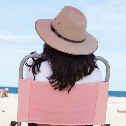 Person sitting on a beach chair wearing a wide-brimmed hat with a scenic background.