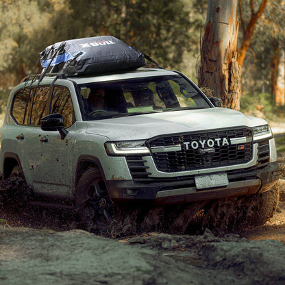 Toyota SUV driving through mud with a roof rack in a forest setting