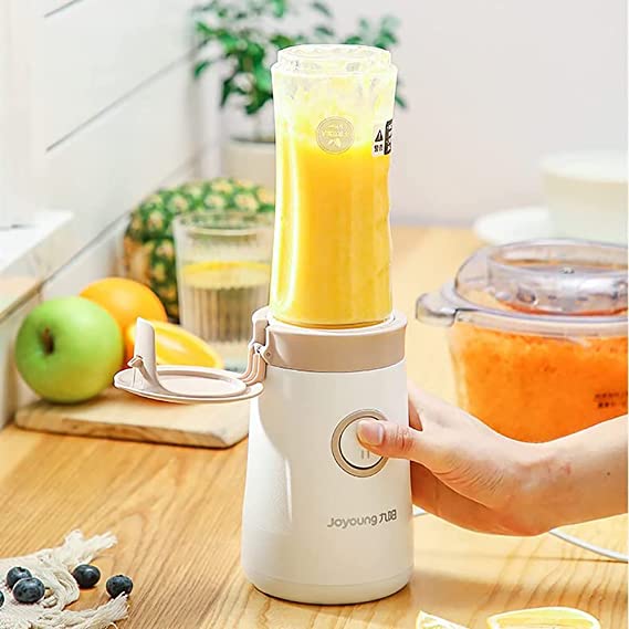 Hand holding a portable blender with a yellow smoothie on a kitchen counter.