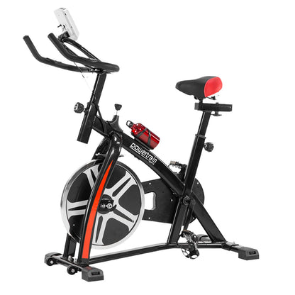 A black Powertrain spin bike with a heavy flywheel, non-slip grip handlebars, and an LCD display screen. It includes a comfortable saddle and an adjustable seat, placed in an indoor setting.