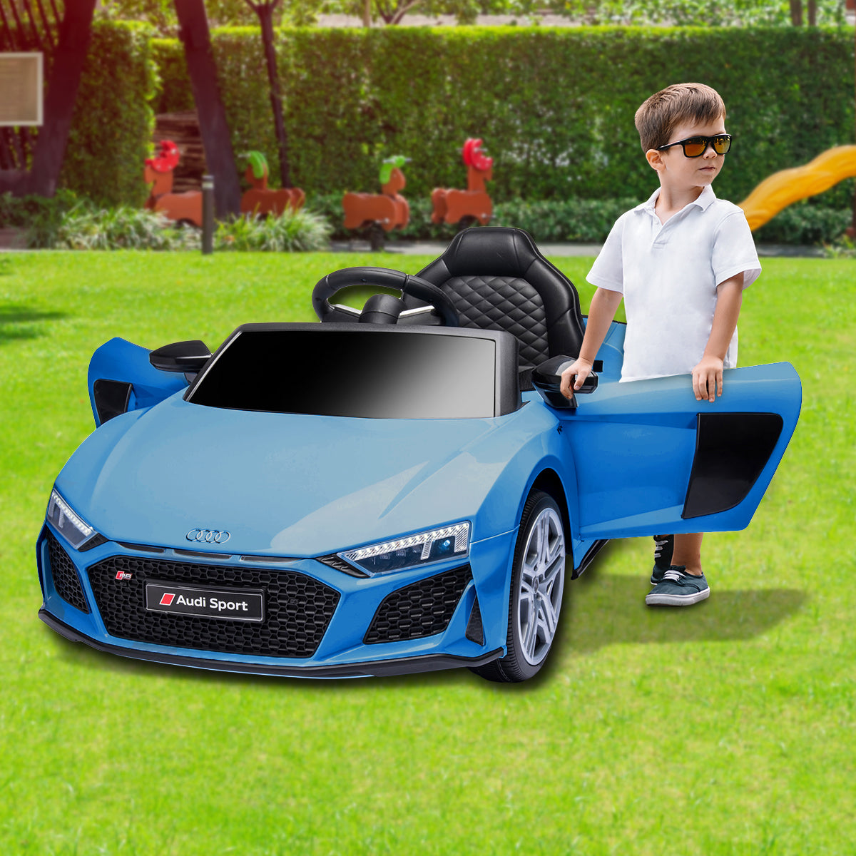 Child standing next to a blue Audi toy car on grass
