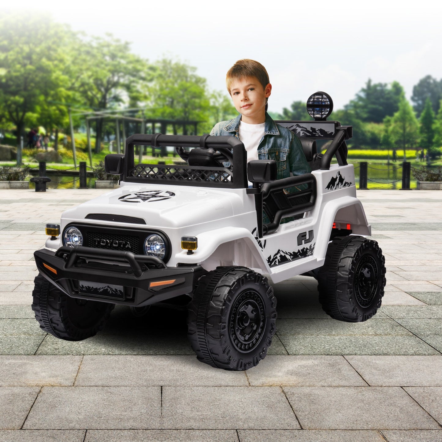 Child sitting in a toy Toyota vehicle on a paved area with greenery in the background