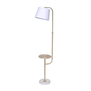 An adjustable floor lamp with a brushed brass finish, marble base, and a metal shelf that doubles as an end table. It has a white tapered lampshade.