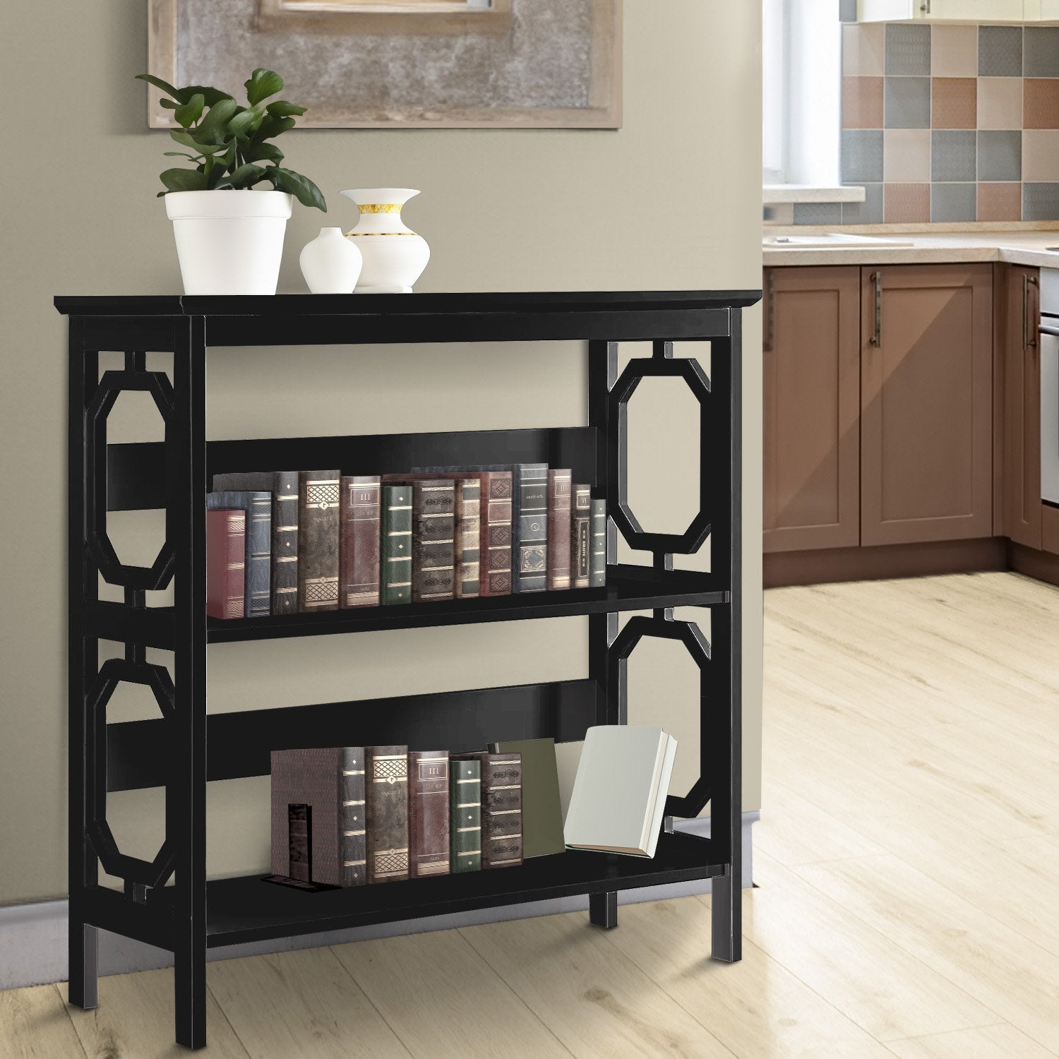 Black bookshelf with decorative items in a room with a kitchen in the background