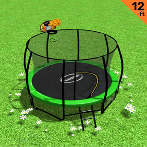 A 12ft outdoor trampoline with a green padding cover, safety enclosure net, black steel frame, and a ladder placed on grass with a toy basketball and hoop set on top.