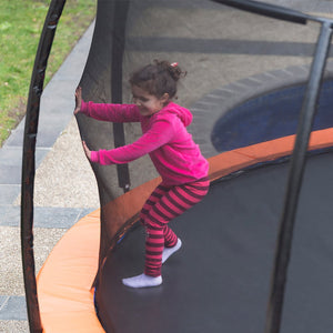A child in a pink top and striped leggings is climbing a trampoline that has a black safety enclosure net.