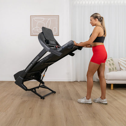 Woman in red shorts and black top using a LifeSpan Fitness treadmill in a home setting.