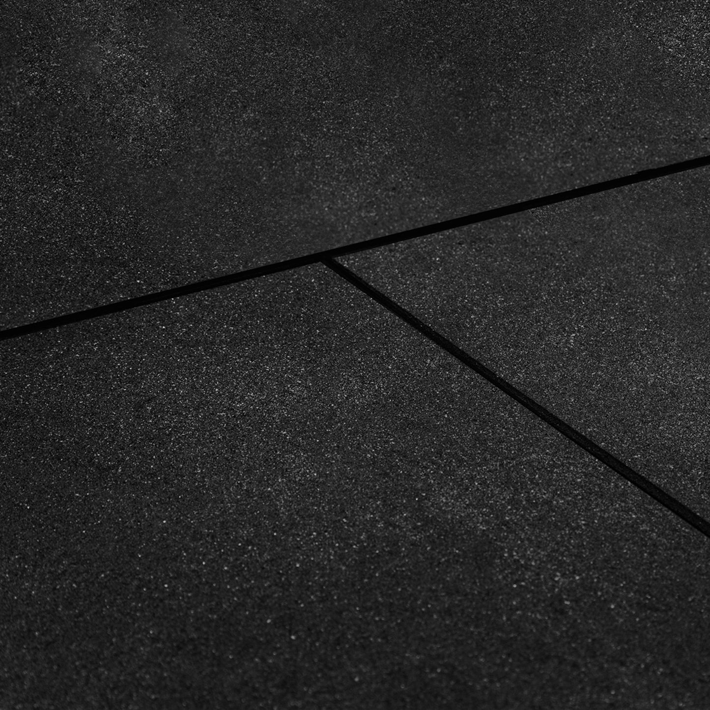 Close-up view of a black  rubber gym tile mat with a bevelled edge, showing the textured surface and slight crevice between mats.
