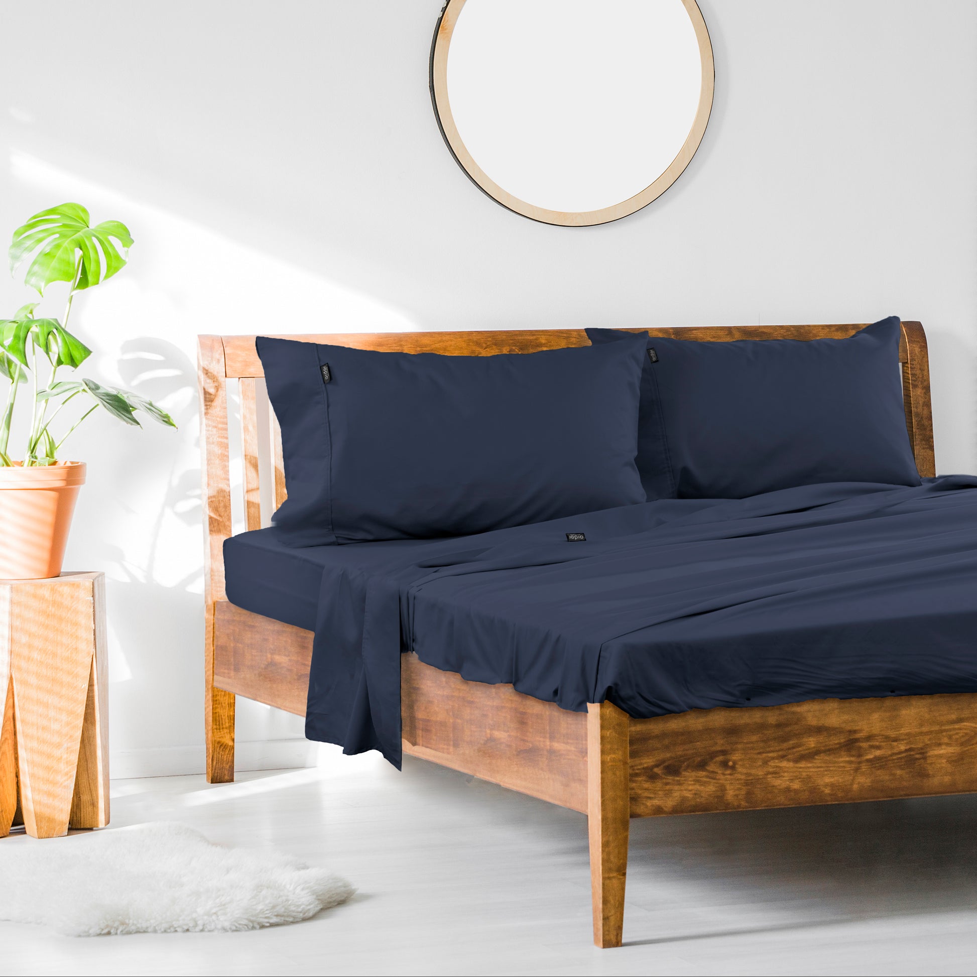 A navy blue cotton rich king sheet set on a bed with a wooden frame, accompanied by a pillow or two and a plant in the background.