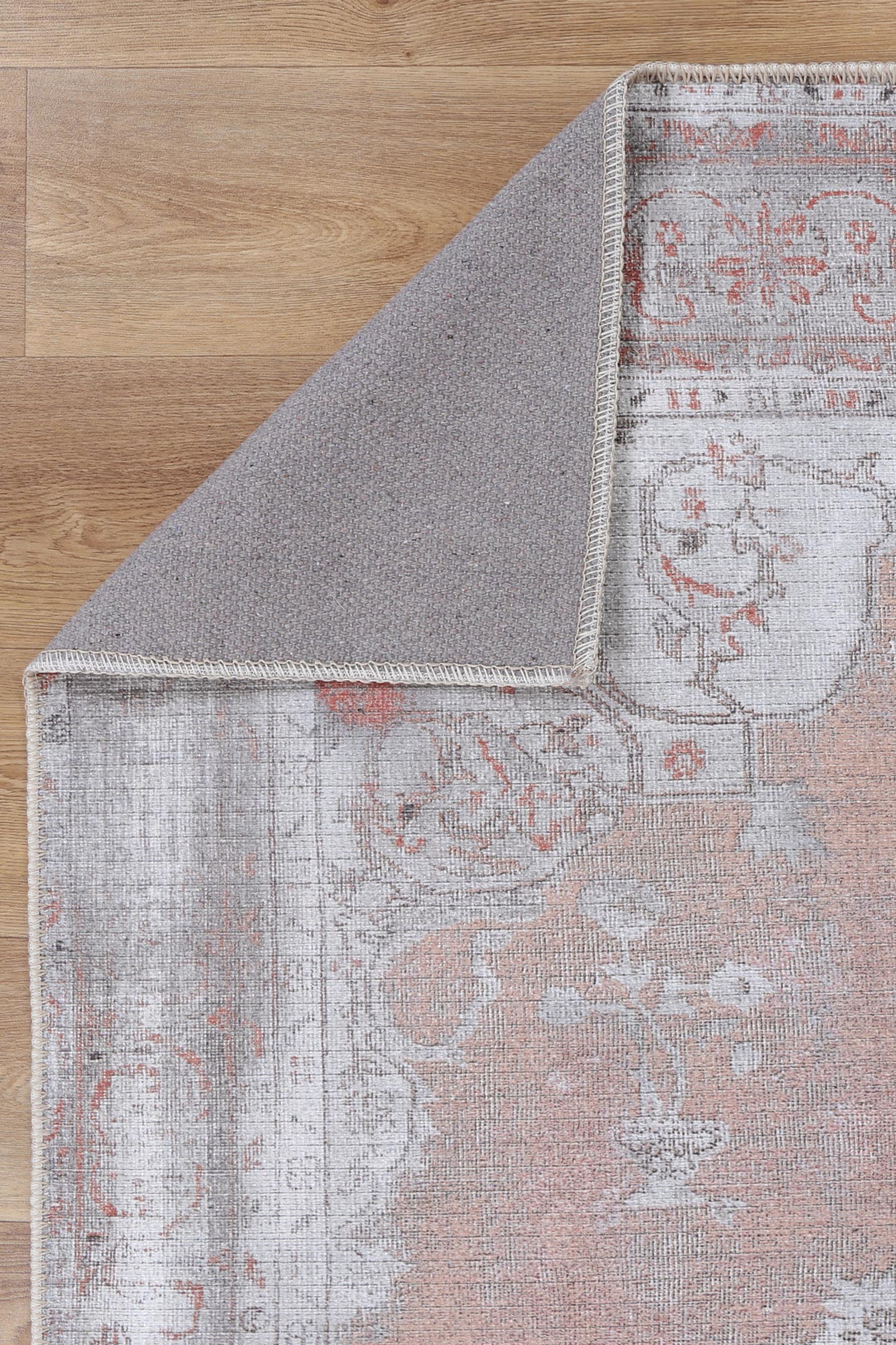 A corner of a machine-washable area rug with a floral pattern in beige, gray, and red colors.